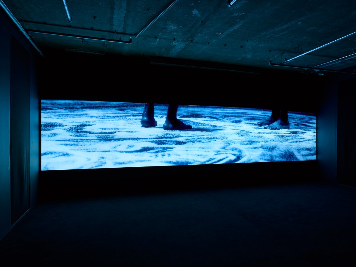 A closeup image of streaks of sand bathed in a blue light, as if someone has been dancing through it