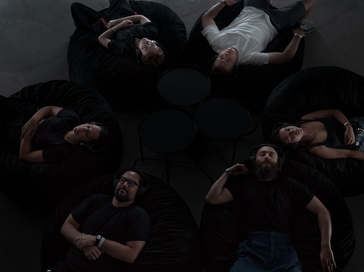 A group of people in a darkened room, lying on their back with their eyes closed, listening to a group meditation